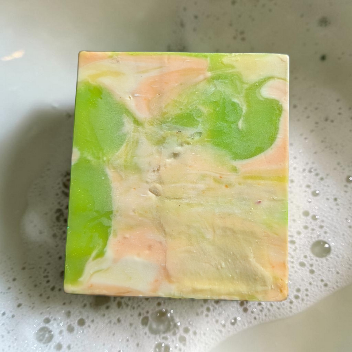 Colorful soap bar with green and pink swirls on a soapy surface